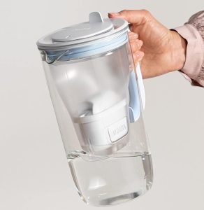 A hand holding a BRITA Glass Water Filter Jug with some water and attempt to poor the water out.