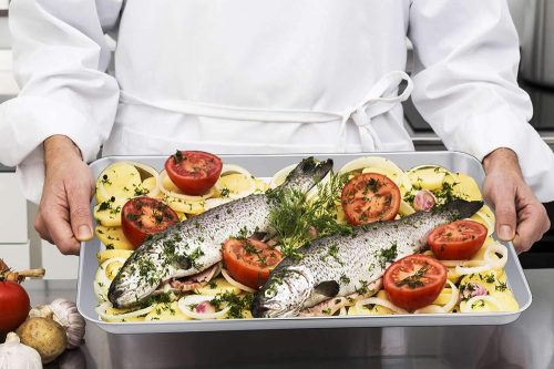 A chef is holding a tray filled with fish, tomatoes and other veggies, ready for baking