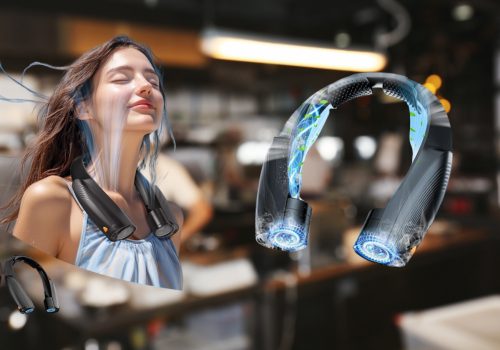 The promotional poster features a woman with long brown hair and closed eyes, seemingly enjoying the airflow from a black portable neck fan worn around her neck. Vapor trails visually represent the cooling effect. To the right, a detailed view of the same neck fan showcases its design and airflow technology. In the blurred background, a chef is preparing his cooking. Another smaller image of the neck fan is visible in the lower-left corner. The overall impression is one of refreshing coolness provided by the portable fan.
